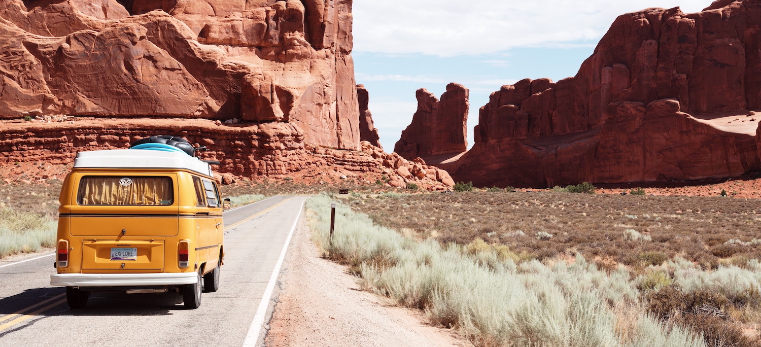 yellow volkswagen van driving by large rocky outcrop