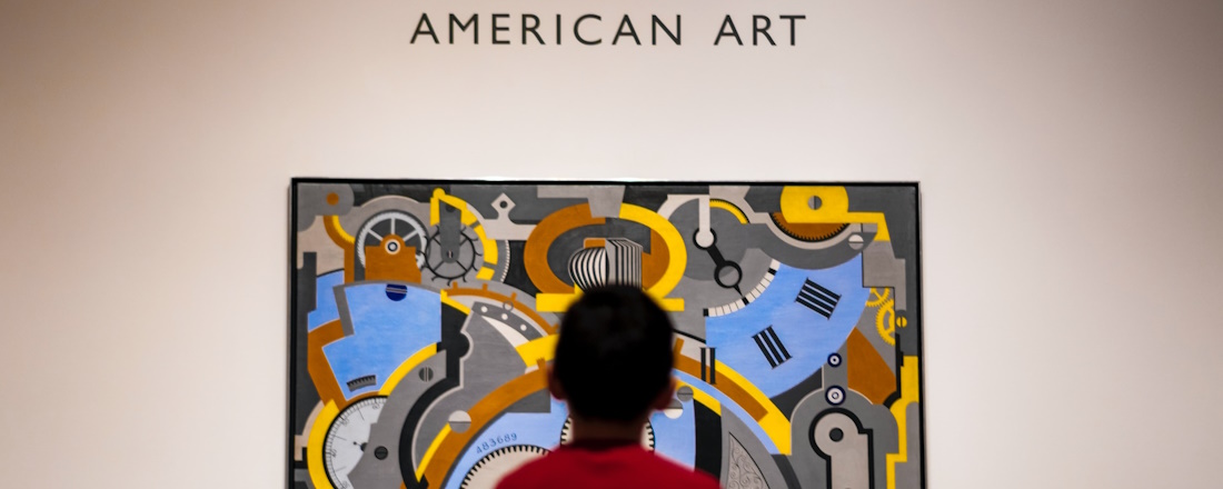 boy in red shirt standing in front of wall with American Art