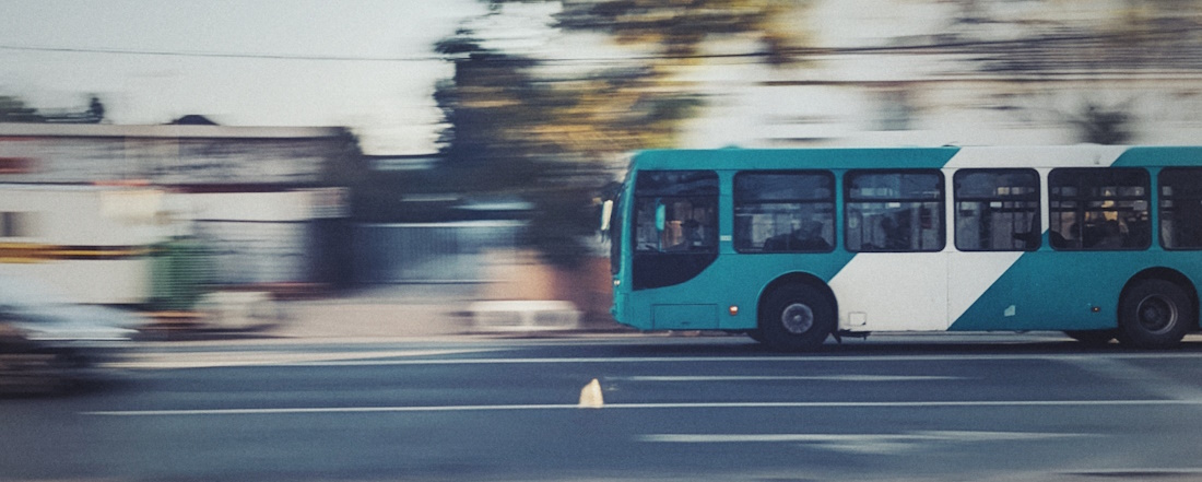 Blue and white bus driving past blurred houses