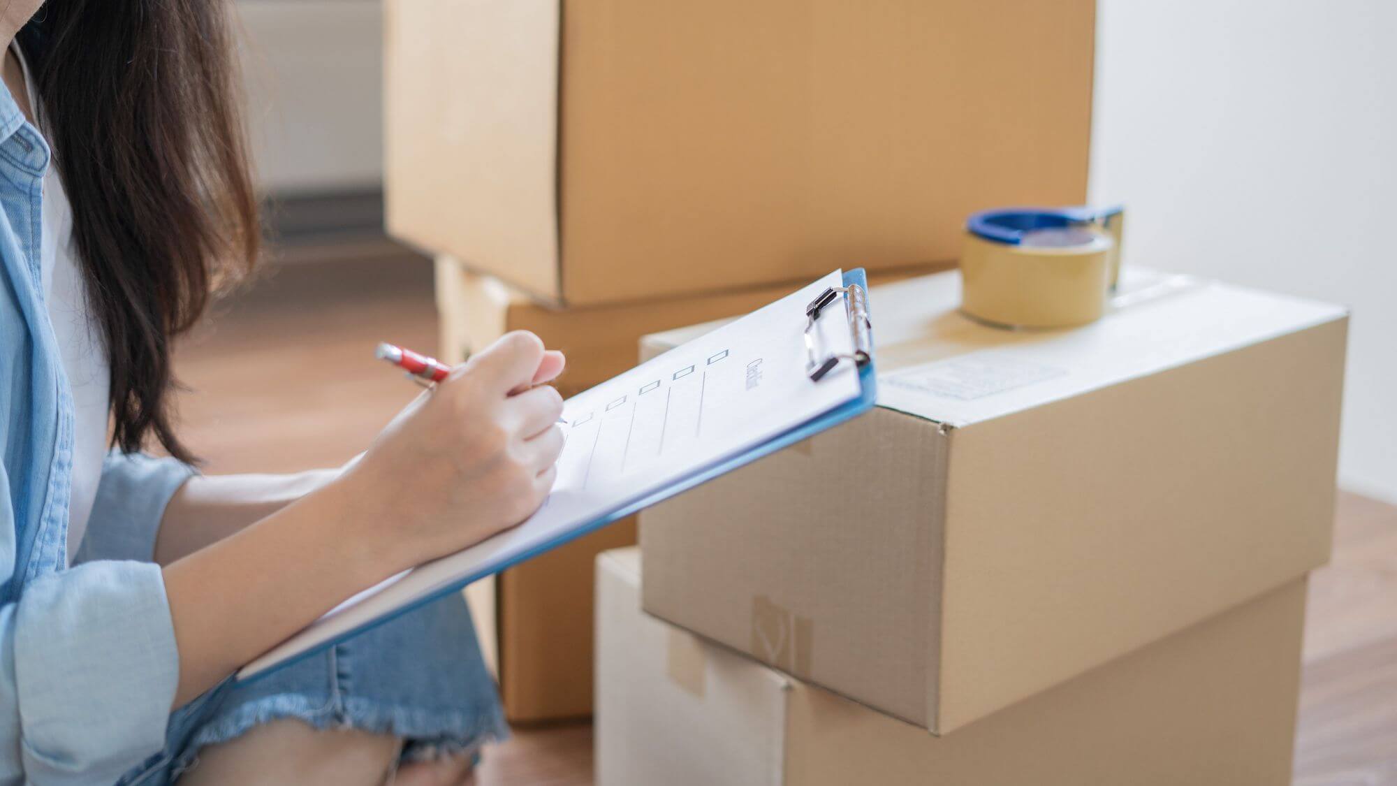 Person checking a checklist on a clipboard in front of moving boxes