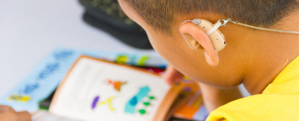 Learner with hearing aid reading colourful book