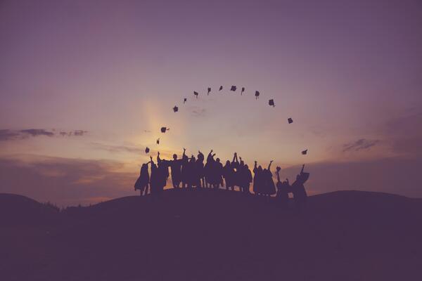 silhouettes of graduates throwing their caps during sunset